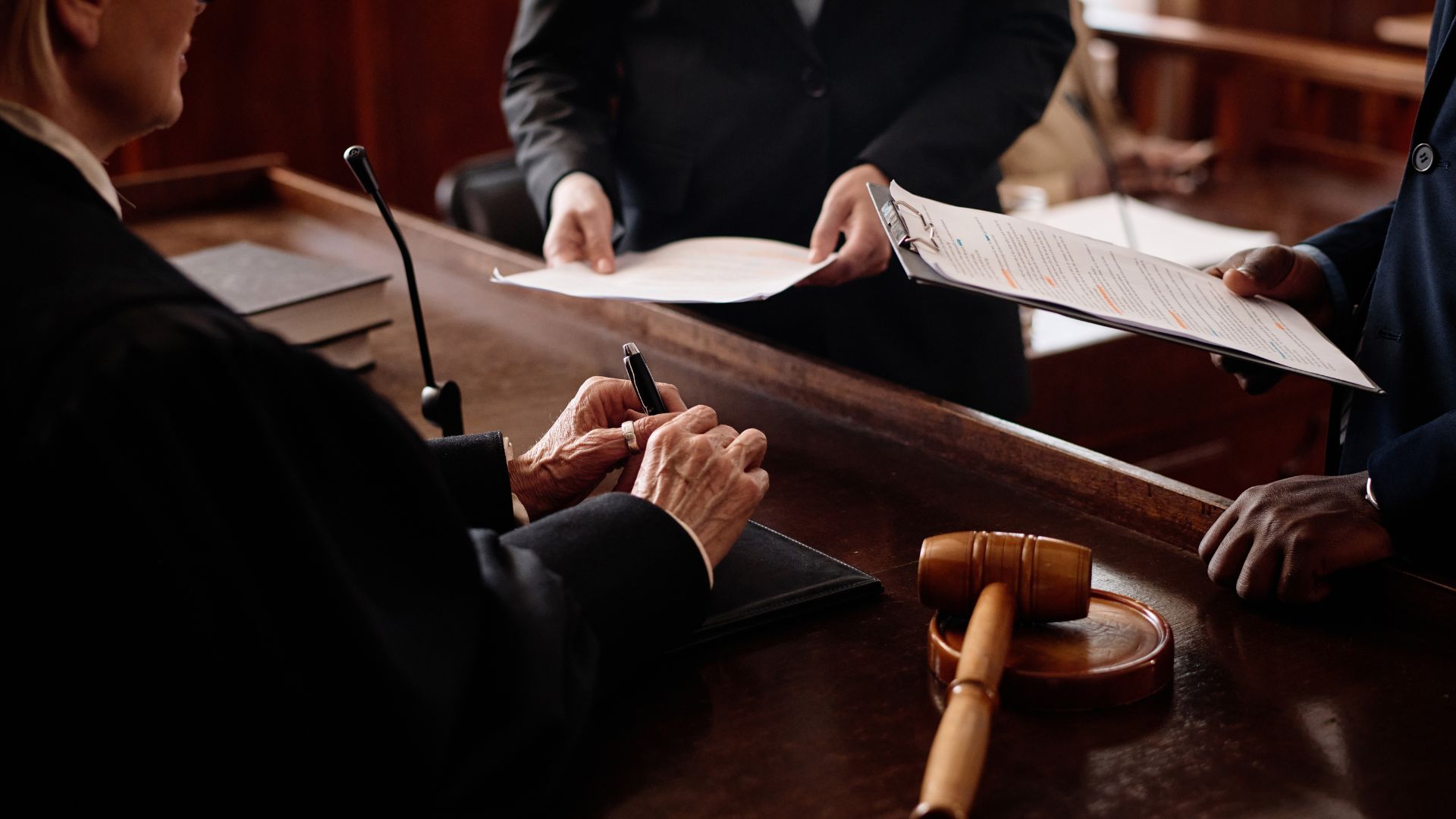 Legal documents being signed at a wooden courtroom desk with gavel