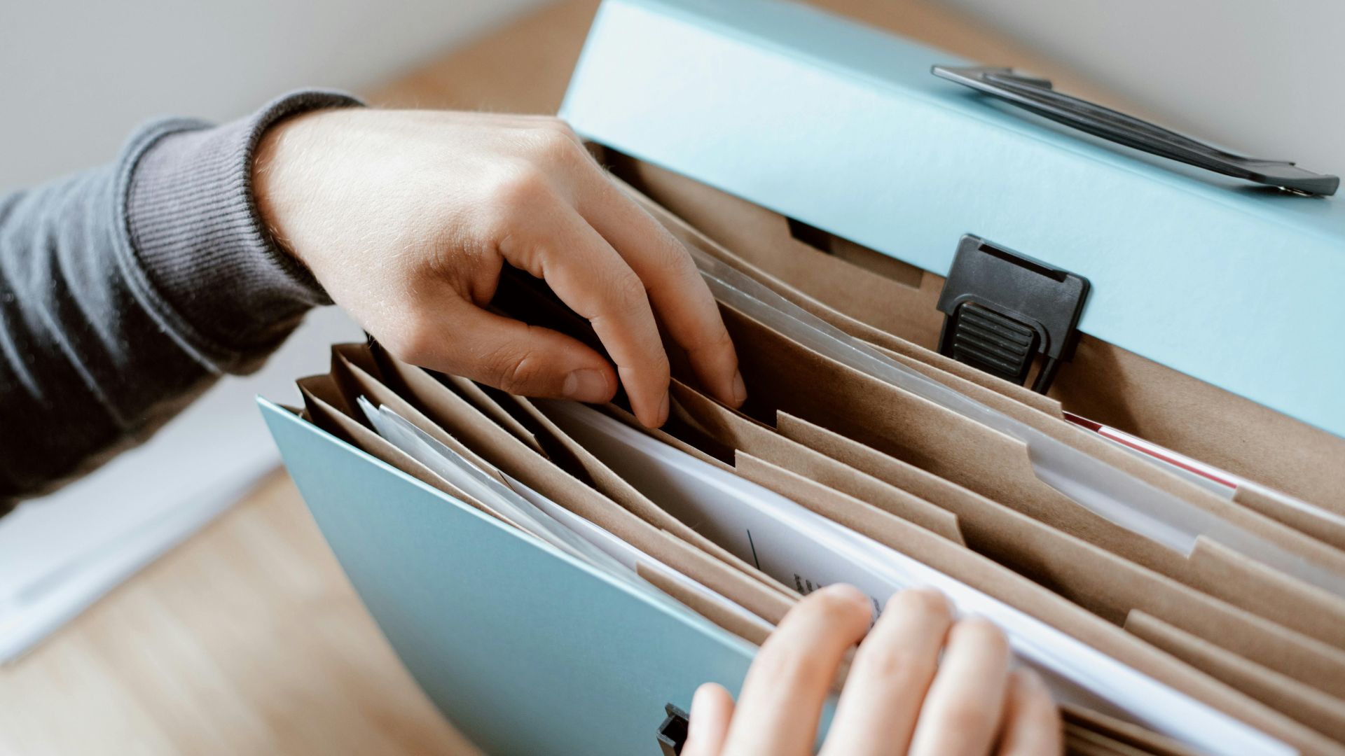 Hands organizing documents in a blue file folder with multiple sections
