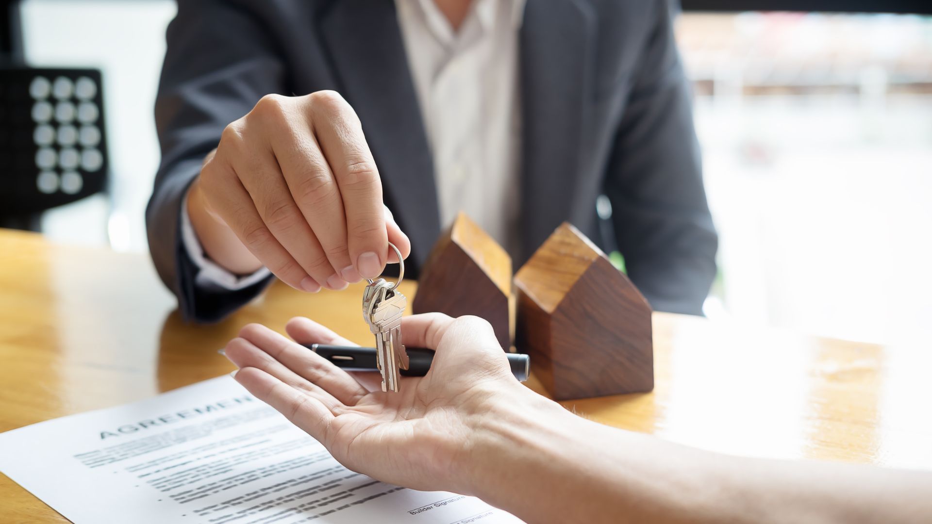 Real estate agent handing over house keys with wooden home models nearby