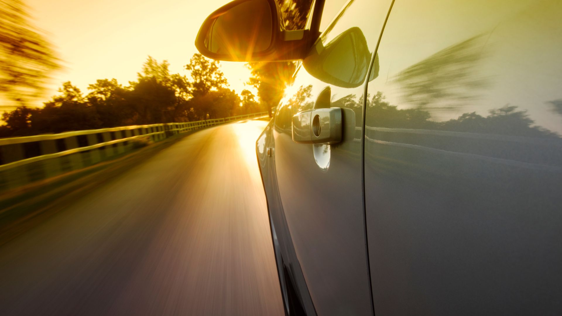 Car driving on highway at sunset with sunlight reflecting on side mirror