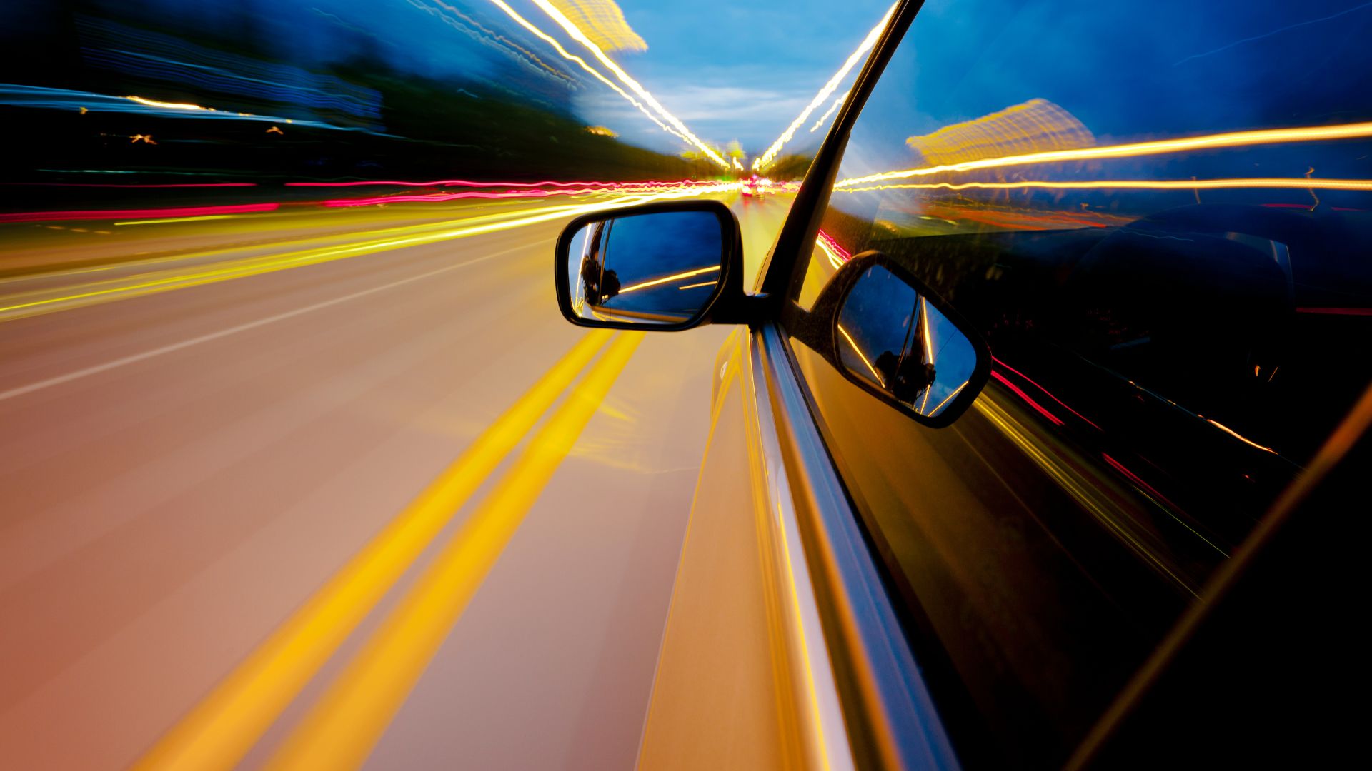 Car side mirror with blurred motion showing speed on highway at night
