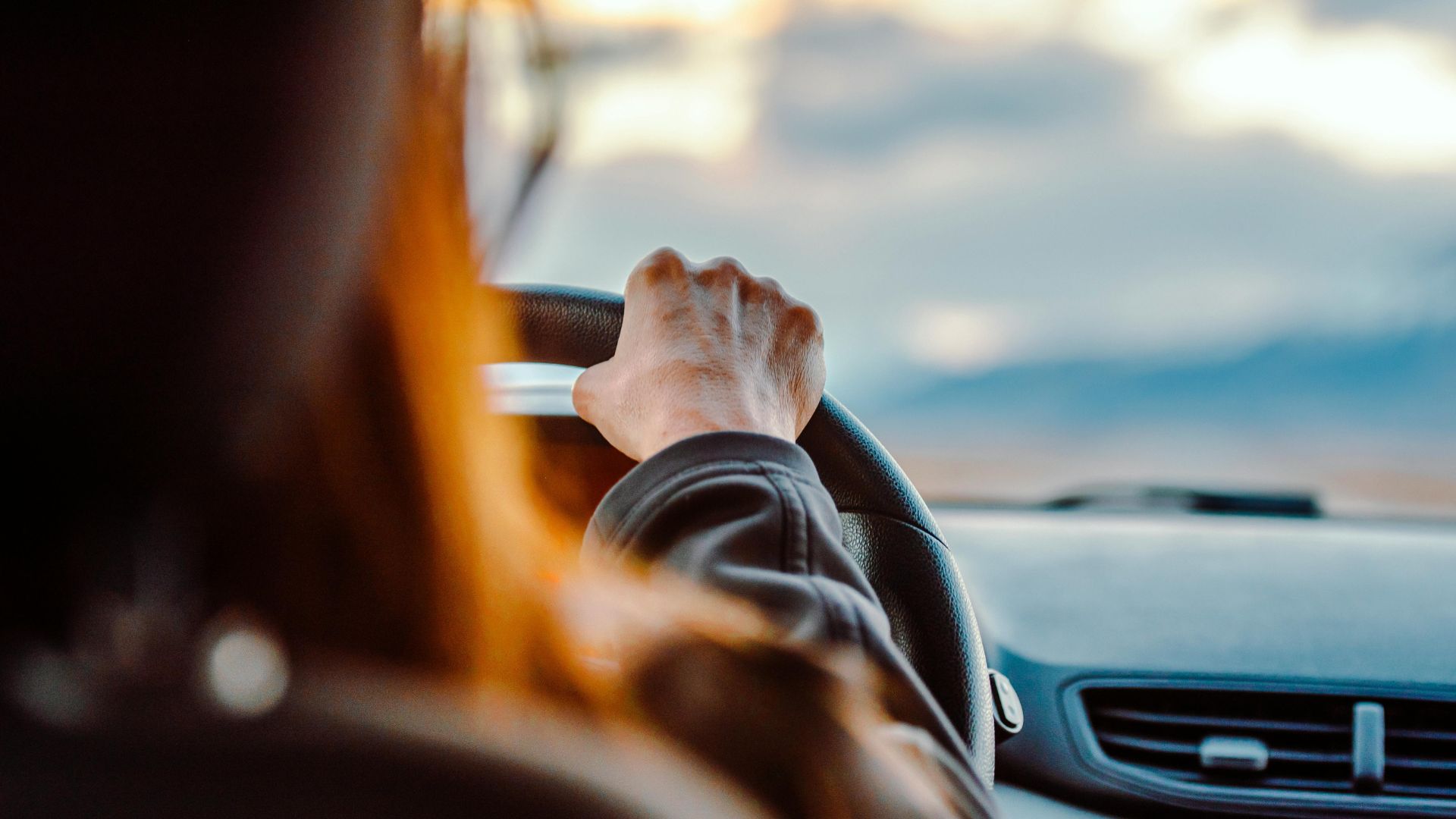 Hand gripping steering wheel while driving with scenic sky in background