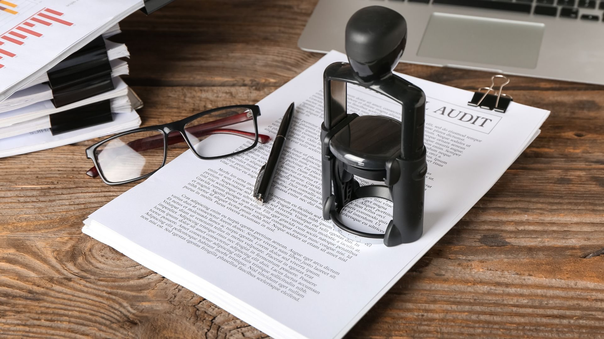Audit document with notary stamp, glasses, and pen on wooden desk